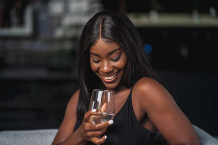 beautiful black girl sitting on her couch holding a glass of wine