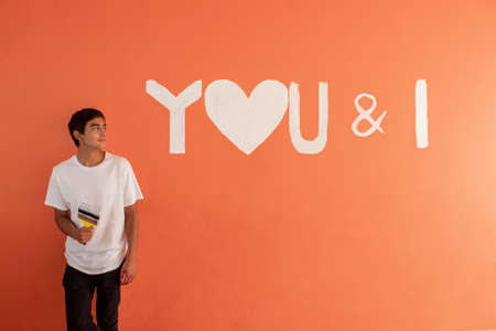 young man paints love note on orange wallの写真素材