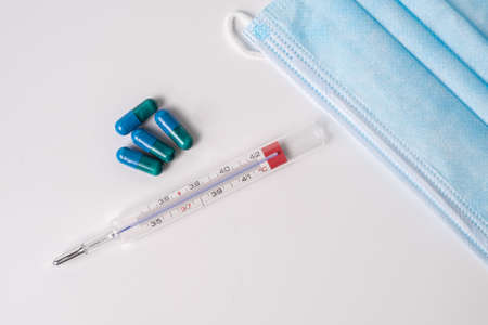 surgical mask medicinal capsules and thermometer on white background