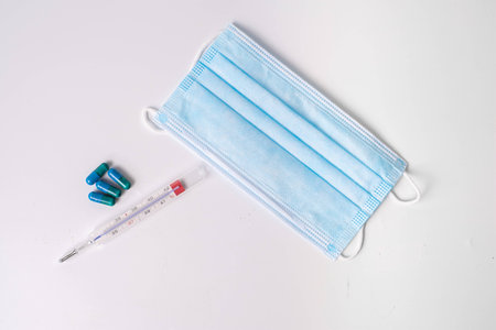 surgical mask medicinal capsules and thermometer on white background