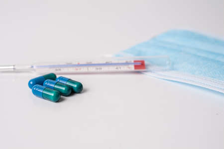 surgical mask medicinal capsules and thermometer on white background