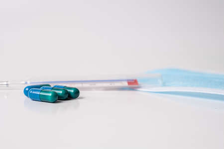 surgical mask medicinal capsules and thermometer on white background