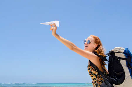 Girl with backpack and paper plane happy at beach