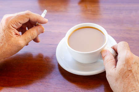 Elderly hand with cup of coffee and cigaretteの写真素材