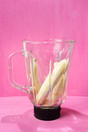 Banana without peel in blender glass jar on colorful backgroundの写真素材