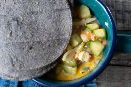 Mexican zucchini stew and blue tortilla on wood background
