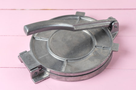 Metallic manual machine tortilla press on wooden pink background