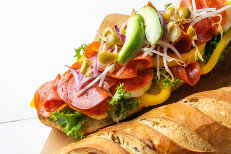 Salami sub sandwich in rustic baguette with avocado, green olives and sproutsの写真素材