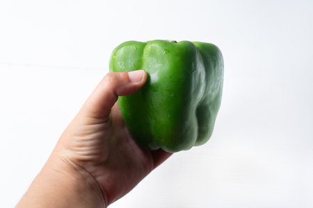 Hand holding green bell pepper on white backgroundの写真素材