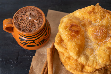 Traditional mexican fritter dusted with sugar also called buÃ±uelos and hot chocolate on dark...