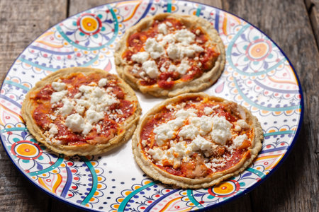 Traditional mexican sopes with red sauce and fresh cheese on wooden background