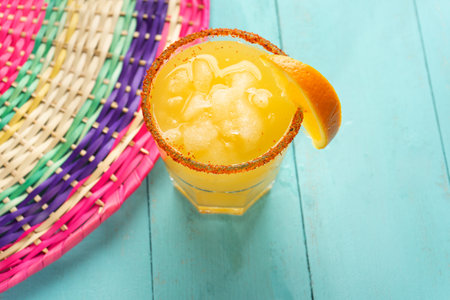 Traditional mexican orange margarita cocktail with chili powder on turquoise background