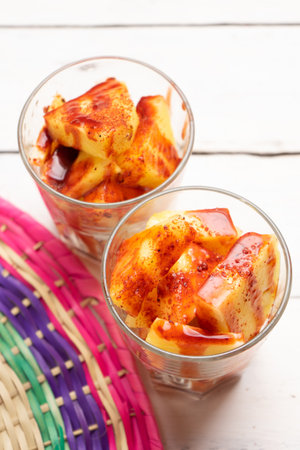 Pineapple fruit cutted with chili powder and piquant sauce in glass on white background