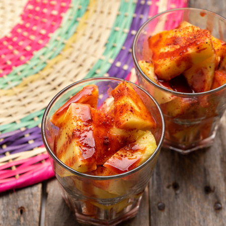 Pineapple fruit cutted with chili powder and piquant sauce in glass on wooden background