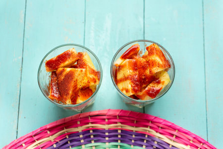Pineapple fruit cutted with chili powder and piquant sauce in glass on turquoise background