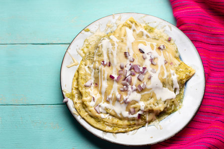 Traditional mexican green enchiladas with melted cheese on turquoise backgroundの写真素材
