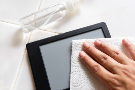 Cleaning ebook reader device with disinfectant in plastic spray bottle on white background