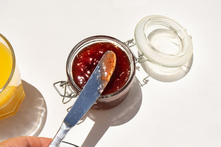 Strawberry jam in glass jar and knife on white backgroundの写真素材