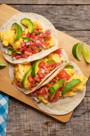 Traditional breakfast egg tacos with flour tortilla and fresh sauce on wooden backgroundの写真素材