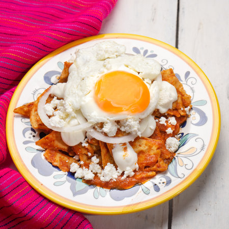 Traditional mexican red chilaquiles with fried egg on white backgroundの写真素材