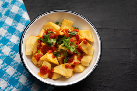 Traditional spanish fried potatoes with sauce also called patatas bravas on dark background