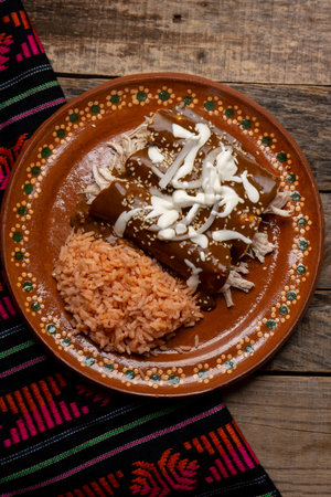 Traditional mexican chicken enchiladas with mole sauce and rice on wooden background