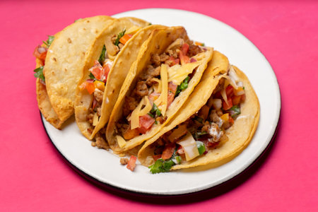 Traditional mexican hard-shell tacos with meat and fresh sauce on pink background
