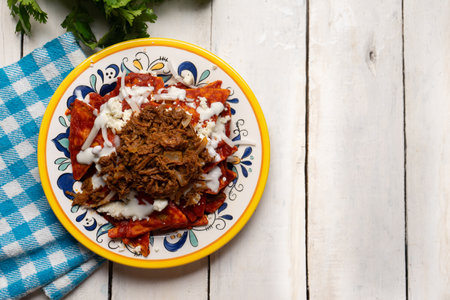 Traditional mexican red chilaquiles with chilorio and cheese on white backgroundの写真素材