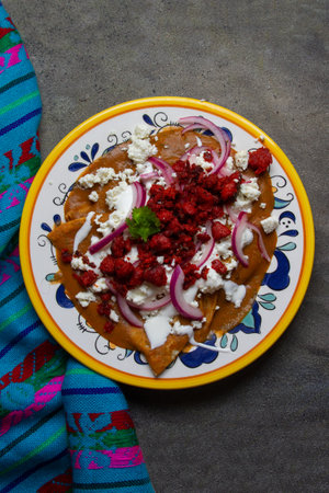 Traditional mexican enfrijoladas with chorizo and cheese on dark background