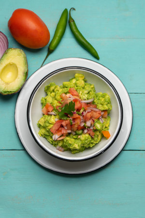Traditional mexican guacamole with chili pepper and tomato on turquoise background