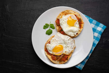 Fried eggs with sauce and tortilla called rancheros for breakfast on dark background. Traditional Mexican foodの写真素材