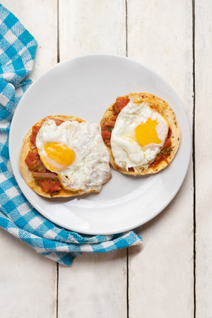 Fried eggs with sauce and tortilla called rancheros for breakfast on white background. Traditional Mexican foodの写真素材