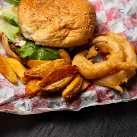 Traditional cheese burger with onion rings and potato fries on dark background
