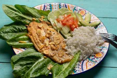 Traditional fish steak with garlic, salad and rice on turquoise background