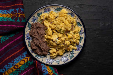 Scrambled eggs with green sauce and refried beans on dark background. Traditional mexican food