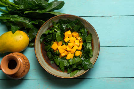 Fresh spinach and mango salad on turquoise background