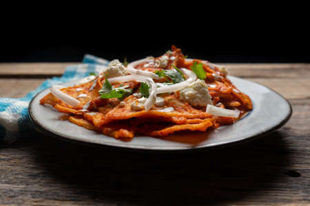Traditional mexican food. Red chilaquiles with cheese and sour cream on wooden background