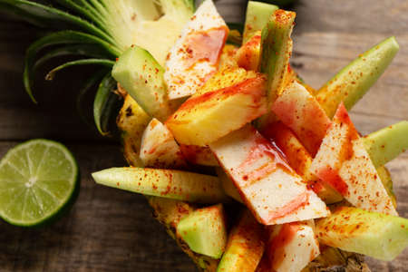 Fresh cucumber, jicama and pineapple with chili powder and chamoy sauce on wooden background. Mexican snackの写真素材
