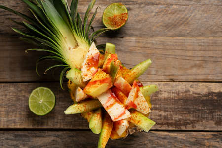 Fresh cucumber, jicama and pineapple with chili powder and chamoy sauce on wooden background....
