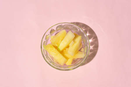 Fresh pineapple cut inside a glass container on a pink backgroundの写真素材