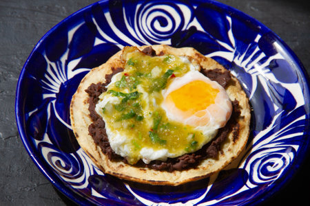 Mexican green ranchero eggs on tortilla toast and refried beans.の写真素材