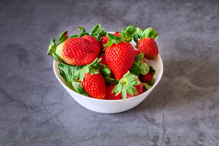 A white bowl with strawberries on a black slate backgroundの写真素材