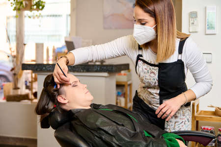 hairdresser doing make-up and styling to young female client in a beauty salonの写真素材