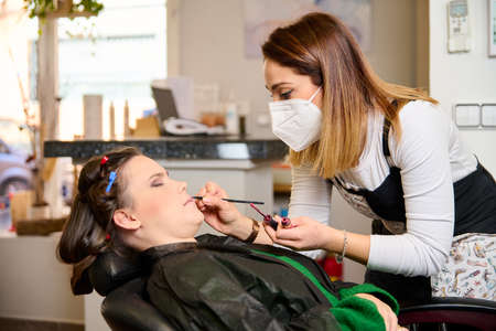 hairdresser doing make-up and styling to young female client in a beauty salonの写真素材