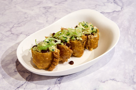 Fried spring rolls on a white plate on a marble background.