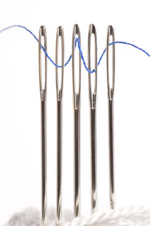 Sewing thread Through the Eye of Five Sewing Needle Isolated on White