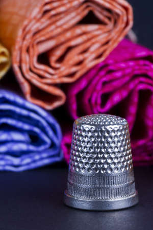 Cylinders of Colorful Fabric and Metal Thimble on Blackの写真素材