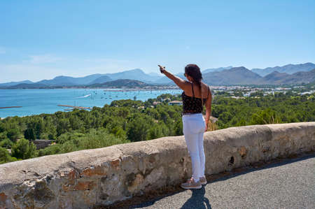 Latin woman, with long wavy brown hair on a spring day wearing sunglasses, on the road with a typical stone wall, indicating where she is, the Pollensa bay, and the base of the hydroplane, against forest fires, in the background Sierra de Tramuntana. Mallorca, Balearic islands, Spain,の写真素材