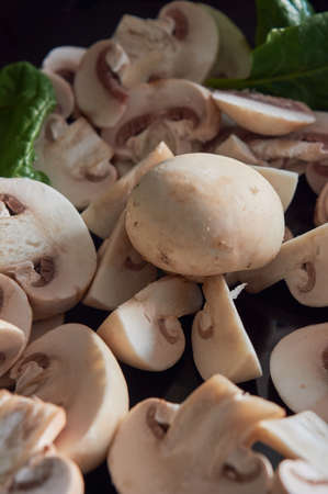 whole and sliced ââmushrooms, on black plate with green spinach leaves, on blue backgroundの写真素材