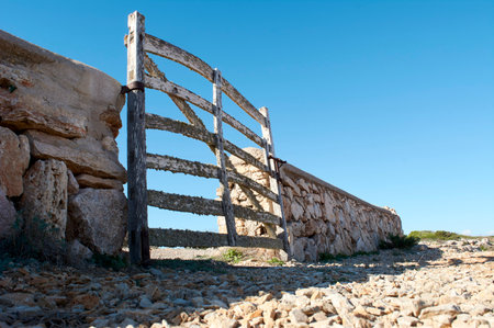 view from the ground, of typical wooden door, with lichens, in stone wall next to the road, with beautiful blue sky over Mediterranean forest, mallorca spainの写真素材